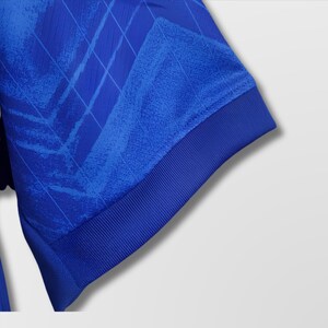 Puede incluir: Primer plano de una manga de camiseta deportiva azul real. La manga presenta un patr&oacute;n texturizado y un pu&ntilde;o acanalado. La tela tiene un brillo sutil y el dise&ntilde;o incluye un patr&oacute;n geom&eacute;trico.