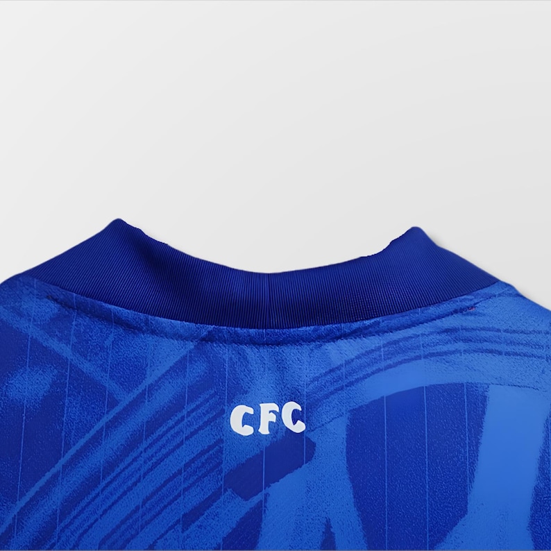Puede incluir: Primer plano de una camiseta azul con cuello azul oscuro. La camiseta tiene un patr&oacute;n texturizado y las letras blancas "CFC" en la espalda. La tela parece ligera.