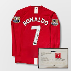 May include: Red long-sleeved football jersey with "RONALDO" and the number "7" in white. The jersey has Barclays Premier League logos on the sleeves and a framed certificate of authenticity.