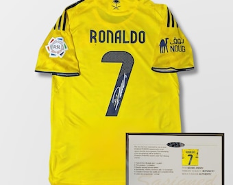 Puede incluir: Una camiseta de fútbol amarilla con el nombre "RONALDO" y el número "7" impresos en la espalda. La camiseta tiene detalles negros y logotipos. Se muestra un certificado de autenticidad al lado.