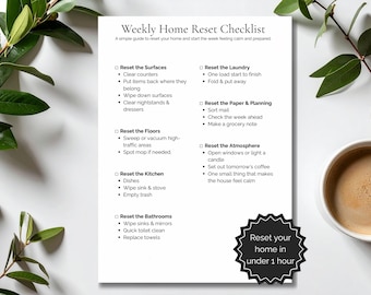 May include: A white printed checklist titled "Weekly Home Reset Checklist" with a simple guide to reset your home. The checklist includes tasks for surfaces, floors, kitchen, laundry, paper, atmosphere, and bathrooms. A coffee cup and greenery are in the background.