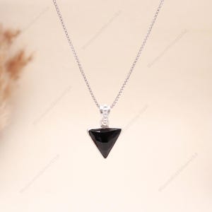 Op de afbeelding: Een zilveren ketting met een zwarte, driehoekige hanger. De hanger is effen zwart en hangt aan een fijne zilveren ketting. De ketting wordt gepresenteerd tegen een neutrale achtergrond.