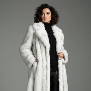 May include: A full-length, white faux fur coat with a wide collar. The coat is worn over a black turtleneck and black pants. The model is wearing black high heels. The coat has a luxurious, textured appearance.