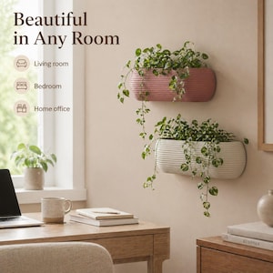 May include: Two wall-mounted planters, one pink and one white, each filled with trailing green plants. The planters have a ribbed texture and are mounted on a light-coloured wall. The text "Beautiful in Any Room" is at the top.