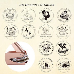 Puede incluir: Una colección de 12 sellos de biblioteca redondos con varios diseños, incluyendo libros, tazas de café y un dragón. Los sellos son de tinta negra, con el texto "FROM THE LIBRARY OF Adriana Flores". También se muestra una prensa de sellos de oro rosa.