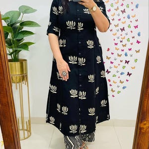 以下が含まれることがあります： 白の花柄が施された黒のロングチュニックドレス。 ドレスはボタンダウンフロントと3/4スリーブです。 お揃いのパンツは、白と黒の幾何学模様のデザインです。 カジュアルまたはセミフォーマルな機会に適しています。