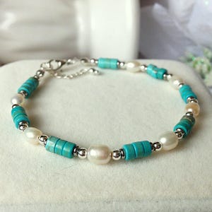 May include: A bracelet with turquoise and white pearl beads, interspersed with small silver-coloured beads. The bracelet is strung on a silver chain with a lobster clasp.