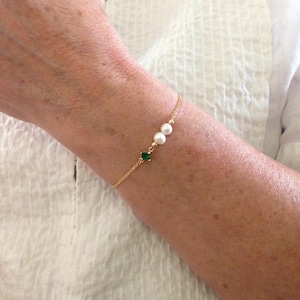 May include: A fine gold chain bracelet adorned with two white pearls and a square emerald-green gemstone. The bracelet's design is simple and elegant, suitable for daily wear or special events.