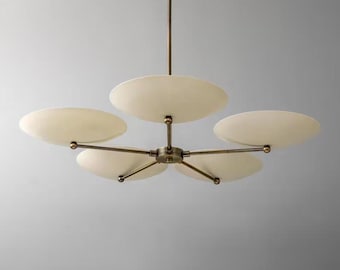 May include: A modern chandelier with five cream-colored, disc-shaped shades. The shades are arranged around a central hub with brass-colored arms. The fixture hangs from a single, slender rod, creating a stylish lighting element.
