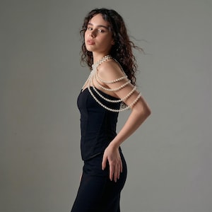 Pode incluir: Um vestido preto com um corpete estilo espartilho e uma saia longa. O vestido &eacute; adornado com uma pulseira de p&eacute;rolas no bra&ccedil;o. A modelo est&aacute; em frente a um fundo cinza.