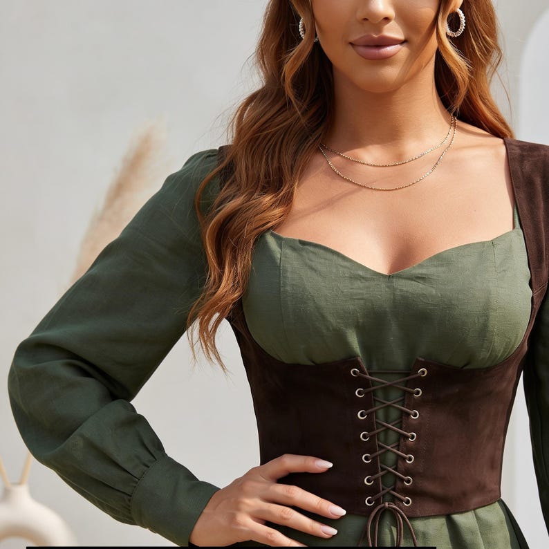 May include: A long-sleeved olive green top featuring a sweetheart neckline and a dark brown corset-style bodice overlay. The bodice is detailed with a vertical lace-up front closure using thin brown cords threaded through silver-toned metal eyelets.