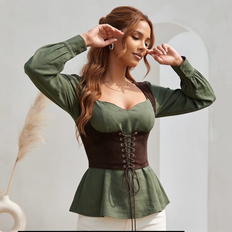 May include: An olive green long-sleeved blouse featuring a sweetheart neckline and a dark brown corset-style bodice overlay. The bodice includes a front lace-up detail with thin brown cords and a peplum hemline that flares at the waist.