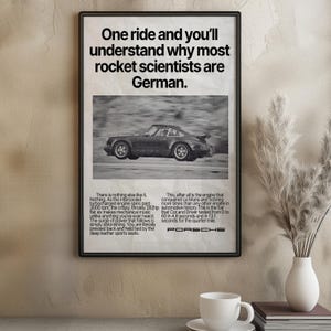 以下が含まれることがあります： 「One ride and you'll understand why most rocket scientists are German」のテキストが入った、黒いフレームのポルシェの広告ポスター。ポスターには、ヴィンテージのポルシェ車の白黒画像が掲載されています。