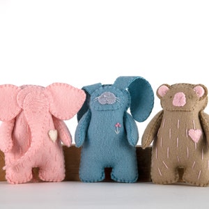 May include: Three felt stuffed toys: a pink elephant, a blue bunny, and a brown bear. Each toy has embroidered details, including eyes, noses, and hearts.