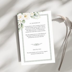 Puede incluir: Una tarjeta conmemorativa blanca con un borde verde y detalles florales. La tarjeta presenta el texto "IN MEMORIAM" y un mensaje de recuerdo. La parte inferior de la tarjeta dice "THANK YOU".