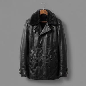 May include: A black leather coat with a faux fur collar hangs on a wooden hanger. The double-breasted coat features two rows of buttons, a notched lapel, and buckle details on the sleeves. The coat is displayed against a gray background.