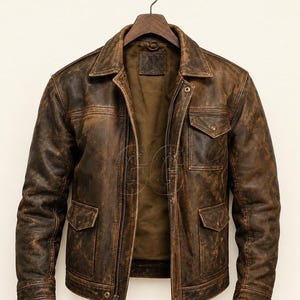 May include: A distressed brown leather jacket featuring a pointed collar, a central zipper closure, and a snap-button placket. The jacket includes two lower flap pockets and one upper chest flap pocket, all with visible stitching and a worn-in finish.