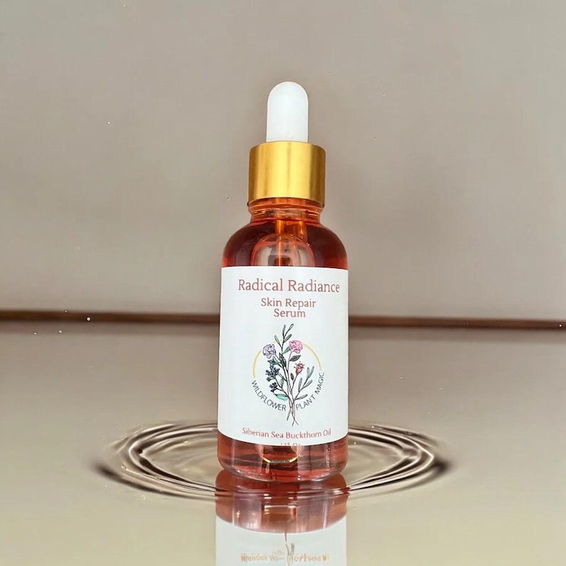 May include: A glass bottle of Radical Radiance Skin Repair Serum with a white label featuring floral illustrations. The bottle has a gold cap and dropper, and the serum inside is a reddish-orange color. The text "Wildflower Plant Magic" is also on the label.