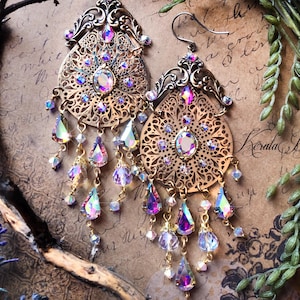 May include: Ornate gold-toned earrings with intricate filigree patterns. The earrings feature iridescent teardrop-shaped crystals and smaller, clear crystals that dangle from the bottom. A large, oval iridescent crystal is set in the center of each earring.