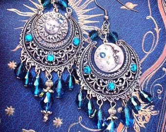 May include: A pair of silver-toned dangle earrings featuring a sun face on one and a crescent moon face on the other. The earrings have intricate filigree metalwork, small teal crystal accents, and multiple dangling dark blue teardrop beads.