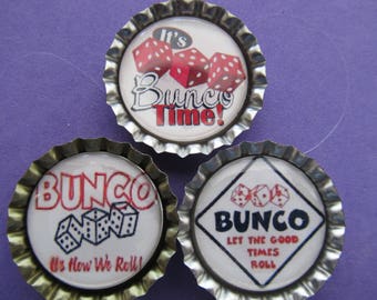 May include: Three silver bottle cap magnets with white backgrounds and colorful dice designs. The first magnet says "It's Bunco Time!" The second magnet says "Bunco It's How We Roll!" The third magnet says "Bunco Let The Good Times Roll!"