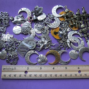 May include: A collection of assorted metal charms including crescent moons with the text I love you to the moon and back, robot figures, and heart shapes, displayed next to a wooden ruler measuring approximately 11 inches in length.