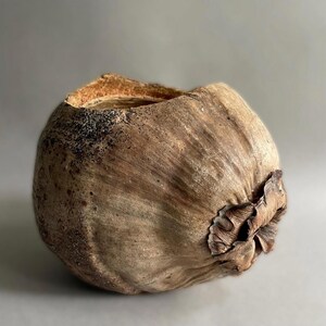 Könnte beinhalten: Eine handgefertigte, kugelförmige, braune Dekoschale mit strukturierter Oberfläche. Die Schale hat ein raues, organisches Aussehen, mit einem dunklen, strukturierten Rand und einem dekorativen, strukturierten Boden. Die Schale besteht aus natürlichen Materialien.