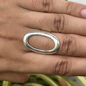 May include: A silver ring featuring an oval design. The ring is displayed on a hand, highlighting its smooth, polished finish. The ring's design is simple and elegant, suitable for various occasions.