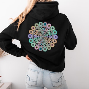 May include: Black hoodie with a colourful gear design on the back. The design features concentric circles of gears in pastel colours, including blue, green, pink, and yellow. The hoodie has a drawstring hood and long sleeves.