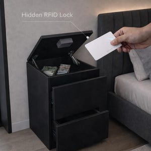 May include: Black nightstand with two drawers and a top compartment, opened to reveal cash. The top compartment has a "Hidden RFID Lock" and is being accessed with a white card. The nightstand is next to a bed.