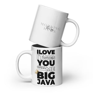 Peut inclure: Deux mugs en céramique blancs. Le mug du bas porte le texte "I LOVE IT WHEN YOU CALL ME BIG JAVA" en noir, avec un motif de couronne dorée. Le mug du haut porte le texte "MORNING HUGS" en gris.