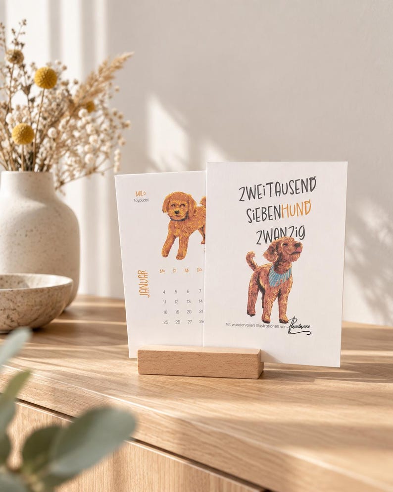 May include: A desk calendar featuring a light wood block stand holding two white cards. The front card displays a brown poodle illustration, the text ZWEITAUSEND SIEBENHUND ZWANZIG, and a signature. The back card shows a January calendar page.