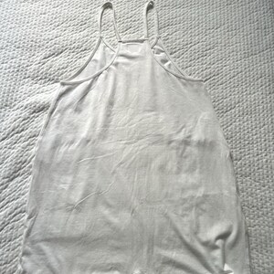 May include: A white romper with thin spaghetti straps and a scoop neckline. The one-piece garment has a relaxed fit and short legs. The fabric appears to be a soft, lightweight material, suitable for warm weather.
