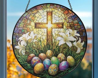 May include: A round stained glass window hanging with a black chain. The design features a gold cross, white lilies, colorful Easter eggs, and green grass against a mosaic background. The window is displayed in front of a blurred outdoor scene.