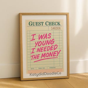 Op de afbeelding: Ingelijste print met een vintage restaurantbon ontwerp. De roze tekst luidt "I WAS YOUNG I NEEDED THE MONEY". Boven staat "GUEST CHECK". De print zit in een houten lijst.
