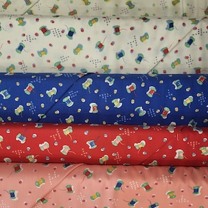 May include: A stack of fabric rolls featuring a repeating pattern of colorful thread spools and cross-stitch designs. The fabrics are in various colors, including white, blue, red, and pink. The spools have green, red, and blue thread.