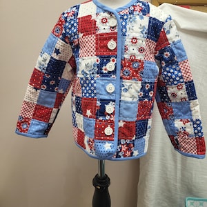 May include: A patchwork jacket in red, white, and blue, featuring a variety of floral and star patterns. The jacket has a round collar, long sleeves, and is fastened with white buttons. The jacket is displayed on a mannequin.