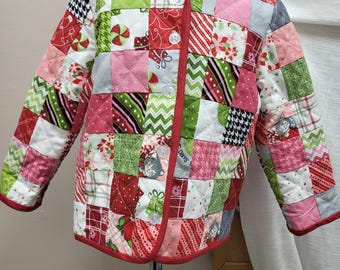 May include: A patchwork quilted jacket in red, green, pink, and white. The jacket has a red trim, long sleeves, and is fastened with buttons. The squares feature festive patterns, suitable for the holiday season.