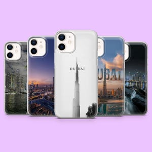Peut inclure: Cinq coques d'iPhone présentant des paysages urbains de Dubaï. Les coques affichent des images de la Burj Khalifa et d'autres monuments, avec le mot "DUBAI" imprimé sur l'une d'elles. Les coques ont une finition brillante, sur fond violet clair.