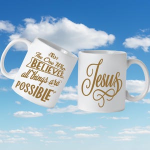 Puede incluir: Dos tazas de cerámica blanca con letras doradas sobre un fondo de cielo azul. Una taza dice "To The One Who BELIEVES, all things are POSSIBLE" y la otra "Jesus". Ambas tazas tienen un asa curva.