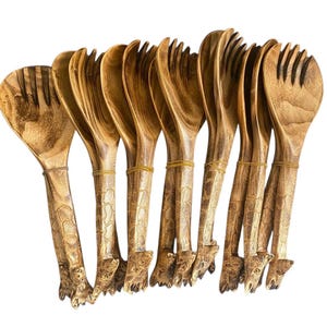 Puede incluir: Un juego de cubiertos para ensalada de madera, que incluye una cuchara y un tenedor, con un acabado de veta de madera natural. Los mangos están tallados intrincadamente con un patrón texturizado y asegurados con bandas de goma.