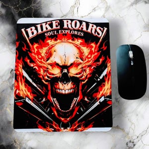 May include: A black mouse pad with a flaming skull graphic and the text "BIKE ROARS SOUL EXPLORES." A black computer mouse is next to the mouse pad. The skull is red, orange, and white.