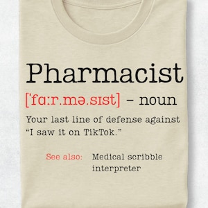 May include: A beige t-shirt featuring black and red text that reads: Pharmacist ['fa:r.mə.sɪst] - noun. Your last line of defense against "I saw it on TikTok." See also: Medical scribble interpreter. The design mimics a dictionary definition entry.