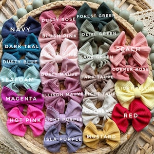 May include: A collection of twenty-four ribbed fabric hair bows in various colors including navy, dark teal, dusty blue, seafoam, magenta, hot pink, dusty rose, blush pink, light pink, dusty mauve, light purple, isla purple, forest green, olive green, sage green, dark taupe, light taupe, oatmeal, peach, copper rose, light yellow, red, and mustard.