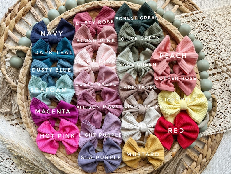 May include: A collection of twenty-four ribbed fabric hair bows in various colors including navy, dark teal, dusty blue, seafoam, magenta, hot pink, dusty rose, blush pink, light pink, dusty mauve, light purple, isla purple, forest green, olive green, sage green, dark taupe, light taupe, oatmeal, peach, copper rose, light yellow, red, and mustard.