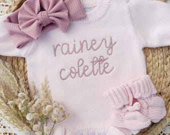 Può includere: Una tutina in maglia a maniche lunghe color rosa chiaro con il nome "rainey colette" ricamato in filo rosa scuro, due bottoni sullo scollo e tre bottoni sul fondo. Include una fascia per capelli a coste color malva abbinata e scarpine.