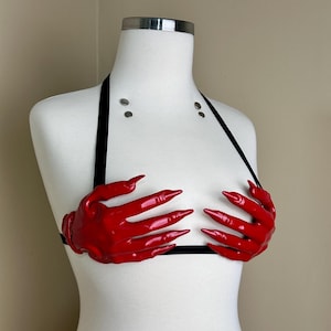Peut inclure: Un haut dos nu compos&eacute; de deux pi&egrave;ces moul&eacute;es en forme de mains rouge brillant aux doigts longs et pointus. Ces sculptures de mains rouges sont fix&eacute;es &agrave; de fines bretelles &eacute;lastiques noires formant un tour de cou et une bande horizontale.