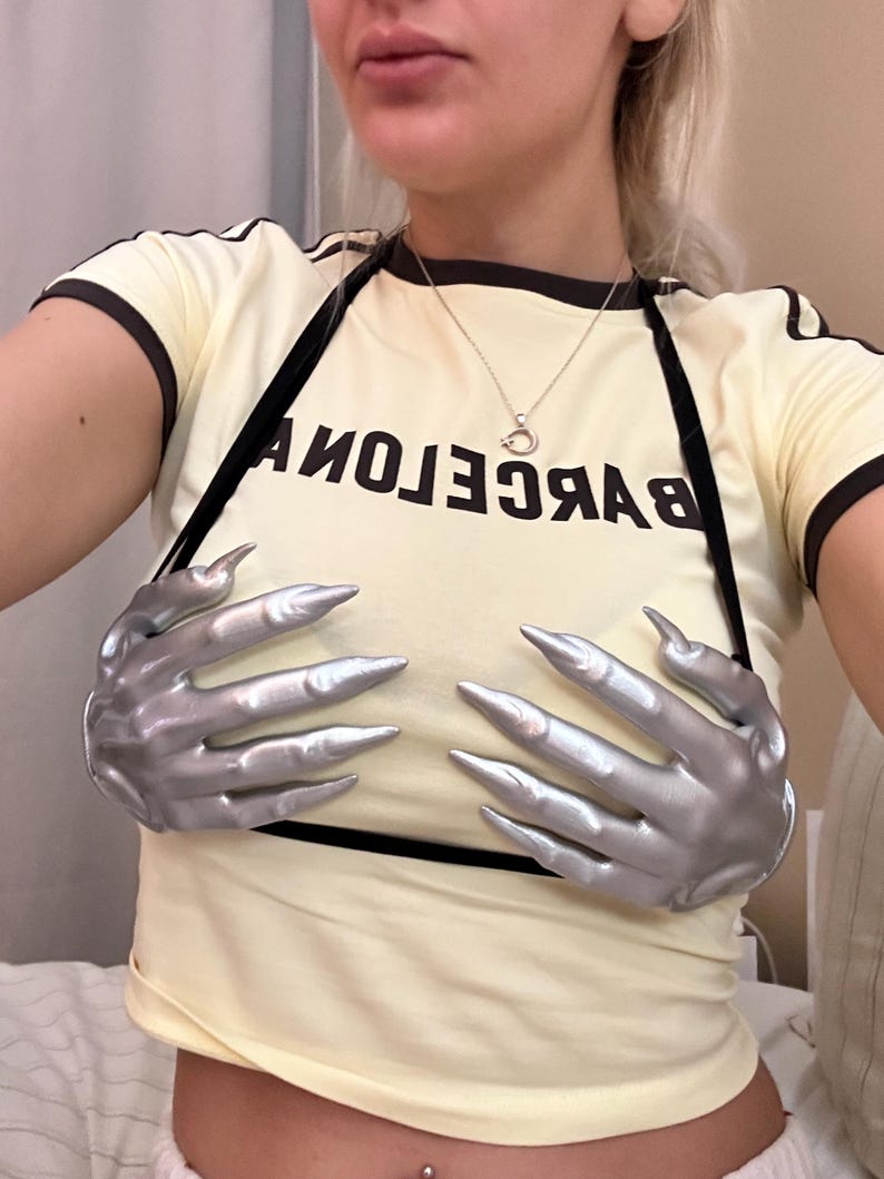 Peut inclure: Un t-shirt &agrave; manches courtes jaune p&acirc;le avec des bordures noires sur les manches et le col. Le t-shirt porte l'inscription BARCELONA en lettres capitales noires et deux grands accessoires en forme de mains argent&eacute;es m&eacute;tallis&eacute;es sur le devant.