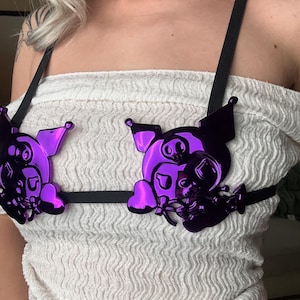 May include: A purple pig-shaped body harness with black straps. The harness has a shiny, reflective surface and is worn over a white, textured top. The pig design includes details like ears, eyes, and a snout.