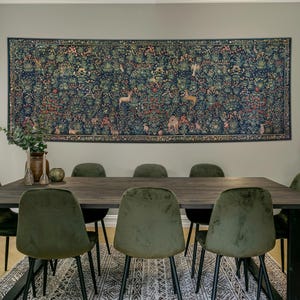 May include: A large rectangular wall tapestry featuring a dark blue background with a dense millefleur pattern of colourful flowers, foliage, and various animals, including deer and birds, displayed above a dark wooden dining table with six chairs.